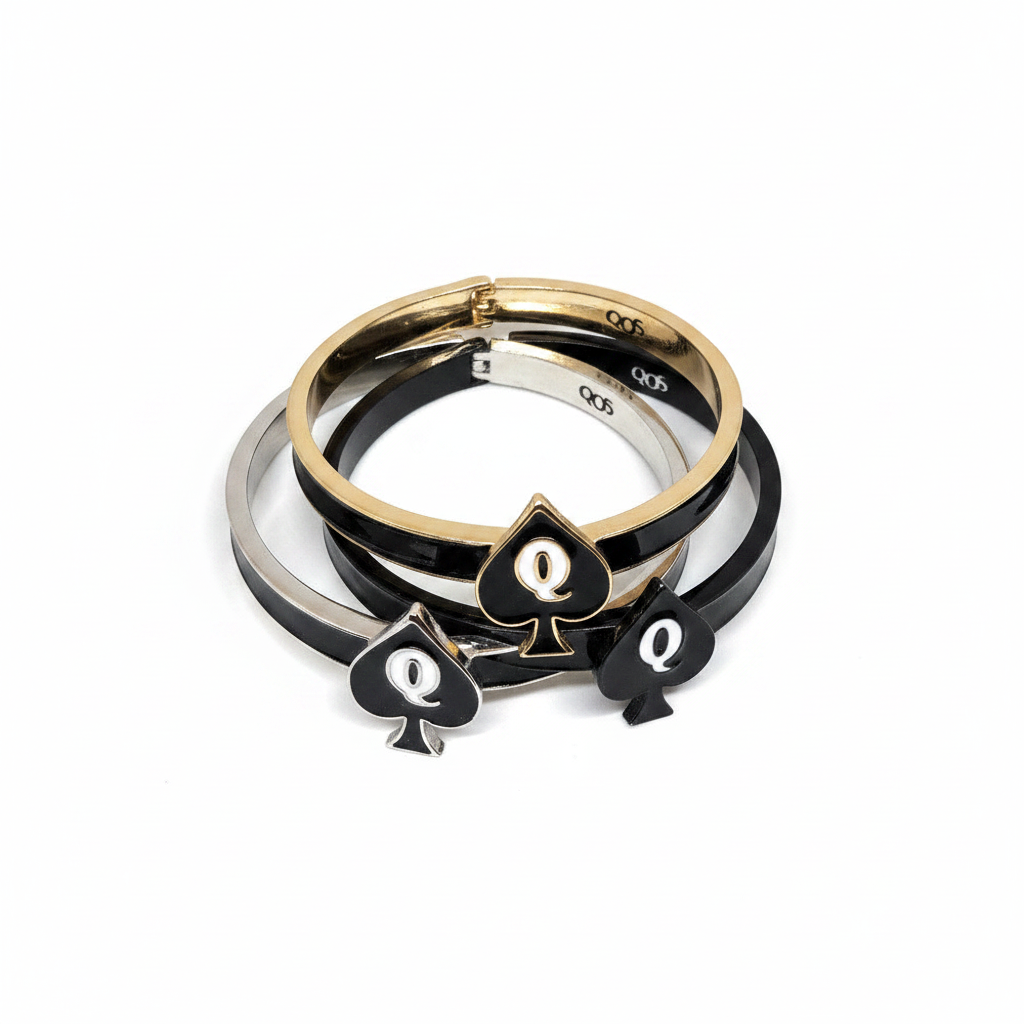 Three stacked bangle bracelets on a white background, featuring black and silver metallic bands with a gold-tone spade-shaped charm in the center.