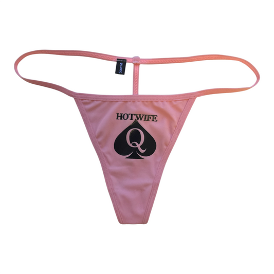 Pink thong-style underwear with a black printed graphic on the front reading 'HOTWIFE' above a large spade containing a 'Q'. A small black brand tag is visible at the back waistband.