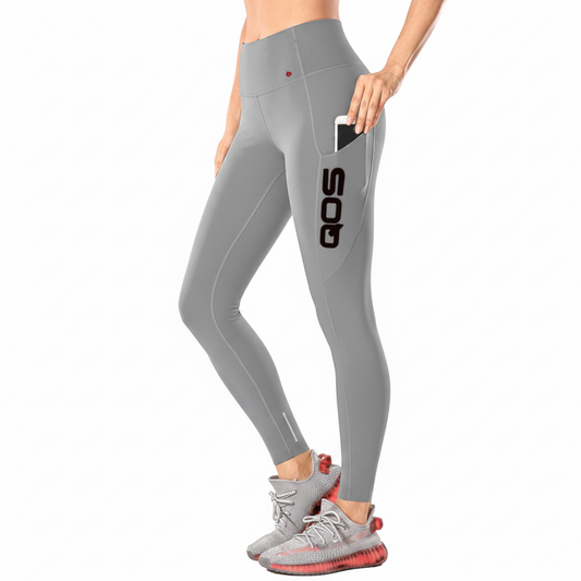 A model wearing light gray high-waisted athletic leggings with a side pocket holding a phone and a large black QOS logo on the upper thigh. The model is also wearing gray running shoes with red soles, set against a plain white background.